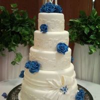 Blue Roses Wrapped With A Bow This fondant covered cake features blue gumpaste roses, lace wraps, a drape wrapped around one tier with a bow. 6" 8" 10" 12...