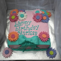 Gerbera Birthday Cake A 10" square vanilla cake covered in white choc buttercream and decorated in brightly colored fondant gerbera's and a bow. This...