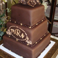 Chocolate Wedding Cake This is a 6,8,10" square cake. Royal icing plaque stencil, with monogram. Painted gold with luster dust. Flowers are handmade and...