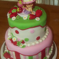 Strawberry Shortcake white cake,bc frosting, fondant stripes, pok-a-dots and strawberries. strawberry shortcake on top is a candle.