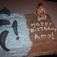 Dolphin_Cake.jpg the cake is 1/2 chocolate and 1/2 yellow. covered with buttercream icing. made the guy out of fondant. the little dog's were just...