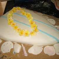 Surfboard With Plumeria And Seashells cake is covered with fondant and surrounded with brown sugar sand. plumeria and shells are gumpaste