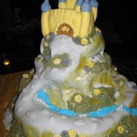 Enchanted Castle Cake Cake is covered in fondant. A cobblestone walk on the mountainside over a river to the castle.