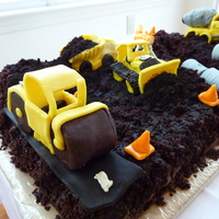 Construction Site Chocolate cake with white chocolate construction vehicles covered with chocolate clay. Road roller compacting a road at one end, while a...