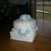 First Stacking Attempt Final cake for a Wilton class. Covered in fondant with fondant roses and draping. The blue flowers are royal icing.