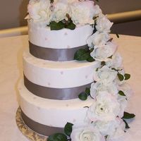 Rose Wedding Cake Buttercream frosting on dummy rounds. Fake flowers cascading down with silver ribbon adorning each tier. The tiers are offset, there is a...