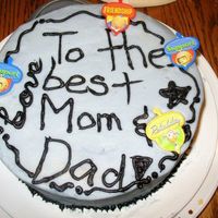 Practice Cake For Mom And Dad A white cake with chocolate filling covered with purple frosting and piped black writing. Plastic decorative rings. A practice cake.