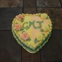 Yellow/orange Heart Heart shaped cake with buttercream frosting and gumpaste flowers and royal icing momongram and fondant leaves on the side (cannot be seen...