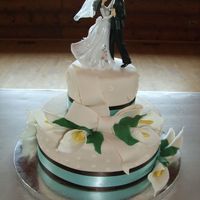 Calla Lilly White almond cakeis iced in buttercream and covered in off-white fondant with gumpaste calla lillies and leaves. The bow is fondant. The...