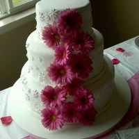 Pink Daisy Wedding 3 Tier cake, covered in white fondant. Real pink daisies adorn the front in a cascade pattern. Small white daisy cutouts are placed on each...