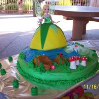 Tinkerbell Tinkerbell standing in a meadow,a lily, mushrooms and a ladybug, and rocks next to a pond. Buttercream, chocolate cake, fondant "...