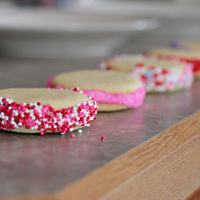 Valentine Cookies Bite size Sugar cookies cut out with the rim of a shot glass with BC sandwiched in between two cookies then rolled in sprinkles