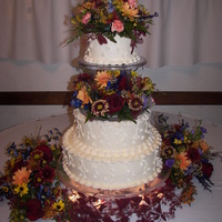Autumn Glow Wedding Cake Piped vines trail over the edges of this buttercream cake. Fresh Fall flowers surround and top the cake. Cake is displayed over 4 inch...