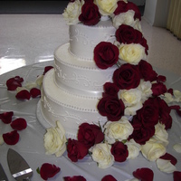 Pearls And Roses Three tier buttercream cake accented with pearls and white satin ribbon. Fresh roses cascade down the cake.