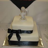 Precious Moments White MMF covered cake tied with a black ribbon and a Precious Moments topper.