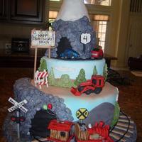 Planes, Trains And Automobiles chocolate cake with ganache filling covered in fondant. train, airplane, cars and bulldozer made of fondant. debris is chopped jelly...