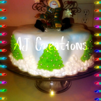 Christmas Cake the top is a snowman ornament. the cake is covered in fondant, the trees and the snow are made with frosting.
