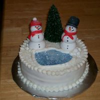 Snowman Cake buttercream cake with fondant snowpeople. Lake is blue fondant with luster dust. The tree is an upsidedown sugar cone piped with...