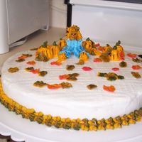 Fall scarecrow sitting in a pumpkin patch. with leaves around. Everything is made out of buttercream