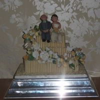 White Chocolate Cigarillo Cake With Models 3 tier square sponge cake with qhie chocolate cigarillos, sugar flower spray and modelled married couple