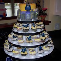 Batman Cake And Cupcake Tower Fondant covered 2 tier cake with Gothman City skyline. Fondant and premade Batman confetti top cupcakes to distinguish the two flavors.