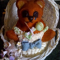 Bear In Basket all edible except basket; bear sits on top of oval cake; rattle and bow fondant; flowers gumpaste