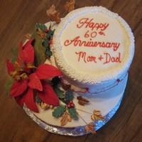 Christmas Anniversary Cake 2 tier Anniversary cake bottom tier white almond, top tier chocolate with buttercream icing. Gumpaste Poinsettia, holly and ivy leaves.