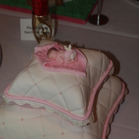 Tiny Miracle Pillow shaped cake layers covered in pink and white fondant accented with fondant lace and rope border. Topped with fondant baby resting on...