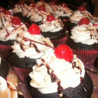 Hot Fudge Sundae Cupcakes chocolate cake filled with hot fudge, topped with vanilla buttercream, peanuts, hot fudge, caramel sauce and a cherry.