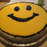 Happy Face 14 inch cake with fondant on top. Face features with black icing. Icing white and yellow flowers around the cake