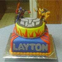 Optimus Prime And Bumble Bee Transformer Cake Chocolate Cake with homemade mmf covering it with mmf accents. Transformers are store bought. This was for a little boy turning 6! TFL