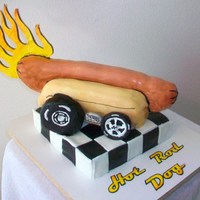 Hot Rod Dog A Company Logo. "Hot Rod Dog" Hot dog on wheelsHot Dog and base are yellow cake. Ends of hot dog are styrofoam. Flames are...
