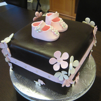 Baby Girl Cake Chocolate cake with caramel buttercream and chocolate ganache filling. Chocolate fondant covering with gum paste flowers and baby shoes....