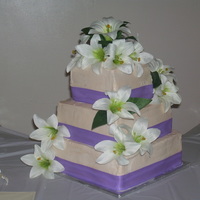 Ivory And Lillies This is an ivory three layer stacked buttercream cake with wisteria colored ribbon and white lillies.