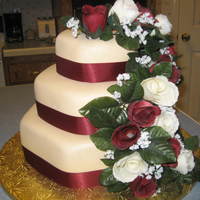 Hexagon Rose Wedding Cake 3 tier yellow cake with buttercream filling covered in ivory fondant. Satin burgundy ribbon and silk roses.