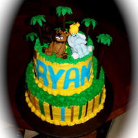 Jungle Safari Baby Shower Cake 12 in cake base, 8 inch cake on top. Cake board covered in brown fondant. Buttercream icing with fondant accents. Jungle animals made from...