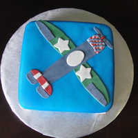 Airplane Single tier, double layer square cake covered in fondant and airbrushed blue. Flat fondant military style plane lying on top.