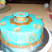 Final Cake For Fondant And Gum Paste Class Covered in blue MMF with brown fondant daisy's and fondant box on top.