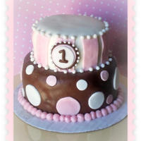 Lily's First Birthday Cake Chocolate and vanilla two tier cake. Covered in White and chocolate fondant. Pink and white fondant accents. "L" wooden letter...