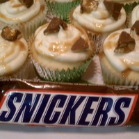 Snickers Cupcake vanilla cupcakes with snickers candy baked in and buttercream frosted with chopped snickers pieces on top.