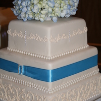 Ivory Scroll Ivory scroll on ivory fondant with blue trim and a rhinestone buckle. Blue fresh hydrangea topper.
