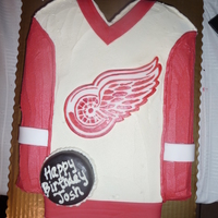 Red Wings Jersey Chocolate Cake, buttercream Frosting. Emblem is fondant with painted on design. Puck is cake with modeling chocolate.