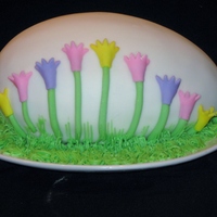 Easter Egg Easter egg cake covered in fondant. Flowers are also fondant. Grass is buttercream using a grass tip.