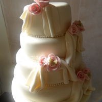 Four Tier Roses And Drapes Wedding Cake Chocolate, lemon and vanilla tiers decorated in ivory icing. Each tier has a pearl border and small clusters of roses with a pearl spray...