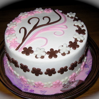 Pink/brown Triple Chocolate latte' cake filled with fudge buttercream. Iced with vanilla latte buttercream, and decorated with fondant accents.