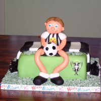 Football Fanatic Sponge cake covered with sugarpaste and figure made partly from marzipan partly from sugarpaste. Grass made from coconut put in a food bag...