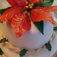 Gumpaste Poinsettia Two tiered white fondant cake topped with a gumpaste poinsettia. Each layer is adorned with a monochromatic fondant rope brushed with gold...