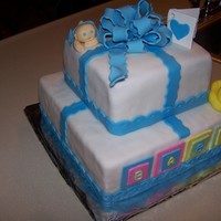Baby Shower Cake Two tiered square cake for a baby shower looks like a gift with the bow on top and the bby crawling under his blanket.