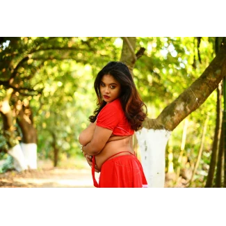 Desi MILF model in vibrant red cropped top and short skirt posing provocatively in lush green forest with confident expression