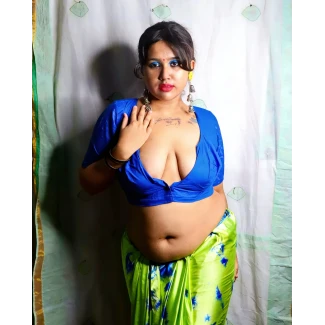 Desi model with full rounded breasts in vibrant blue low-cut blouse showing cleavage and tattoos on chest wearing patterned saree in indoor setting